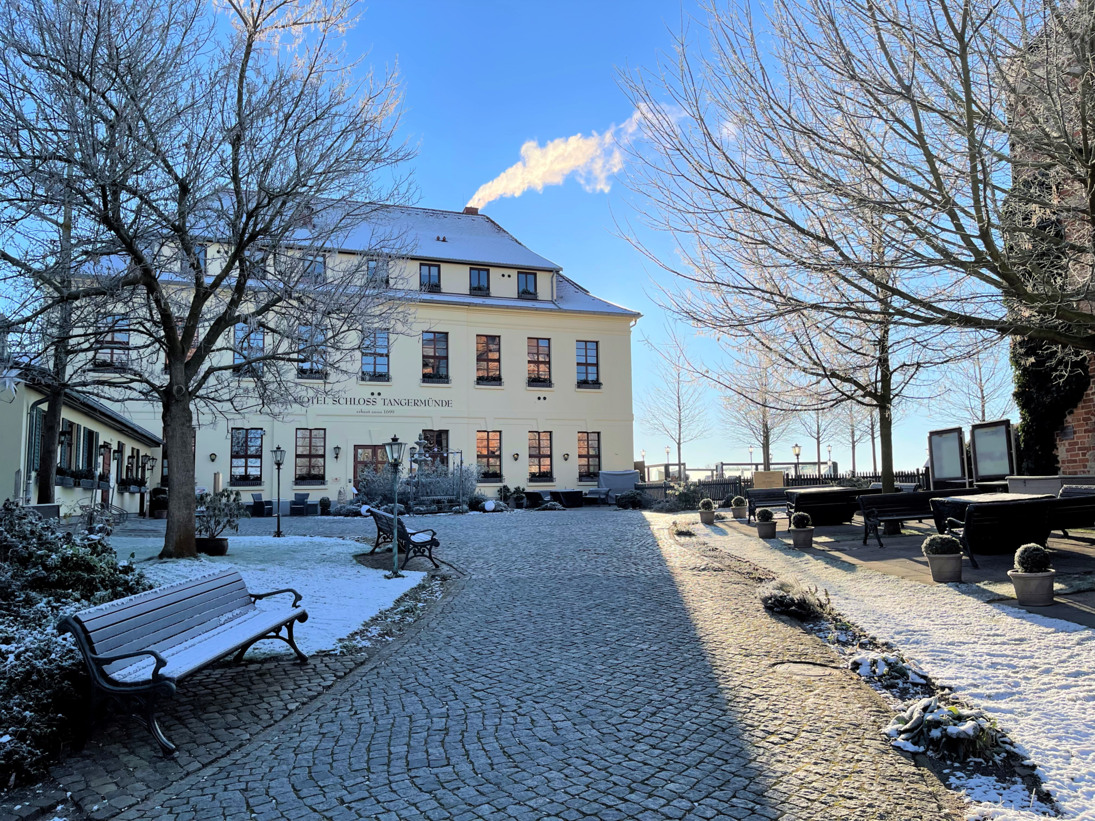 Hauptgebäude des Hotel Schloss Tangermünde im Winter. Schnee/ Reif liegt auf dem Hoteldach und der Bank sowie dem Rasen.